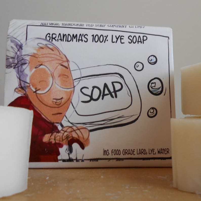 Pu&ograve; includere: Una scatola bianca con un'illustrazione di cartone animato di una donna che tiene una saponetta. La scatola riporta "Grandma's 100% Lye Soap" e "Ing. Food Grade Lard, Lye, Water".