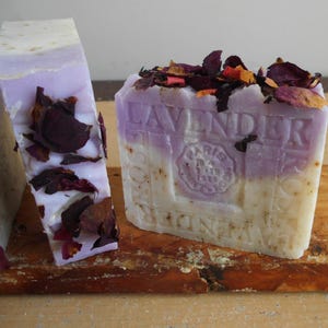 Puede incluir: Dos pastillas de jab&oacute;n rectangulares con un dise&ntilde;o bicolor en blanco y lavanda. El jab&oacute;n presenta p&eacute;talos de flores secas incrustados en la parte superior y los laterales, con el texto en relieve LAVENDER y PARIS 1879 en el frente.