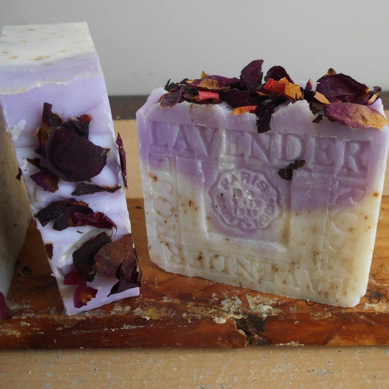 Puede incluir: Dos pastillas de jab&oacute;n rectangulares con un dise&ntilde;o bicolor en blanco y lavanda. El jab&oacute;n presenta p&eacute;talos de flores secas incrustados en la parte superior y los laterales, con el texto en relieve LAVENDER y PARIS 1879 en el frente.