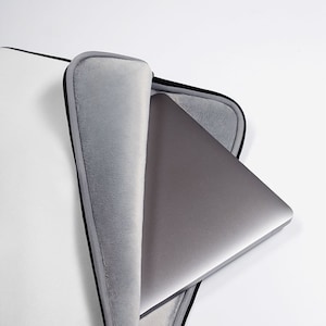 May include: A gray laptop computer is inside a white laptop sleeve with a black zipper. The sleeve has a soft gray lining.