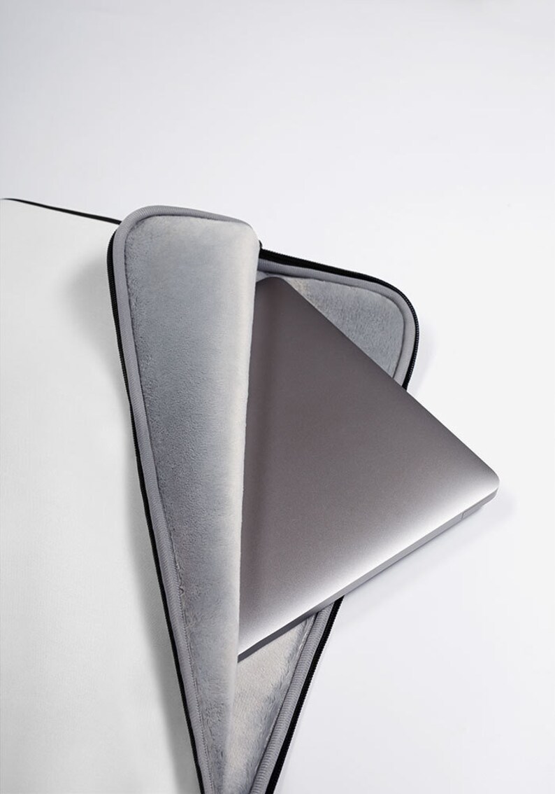 May include: A gray laptop computer is inside a white laptop sleeve with a black zipper. The sleeve has a soft gray lining.