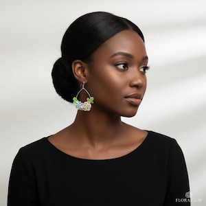May include: Silver hoop earrings with miniature, colourful succulent designs. The earrings feature a delicate arrangement of green, pink, and blue floral elements, creating a botanical-inspired accessory. The earrings are a unique piece of jewellery.