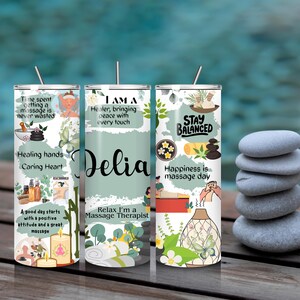 Op de afbeelding: Drie roestvrijstalen bekers met rietjes, met massage-thema ontwerpen en tekst. De middelste beker heeft de naam "Delia" in script. De andere bekers hebben zinnen als "Healing Hands". Een stapel grijze stenen staat op de achtergrond.