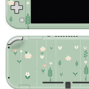 May include: A mint green handheld gaming console with a floral design. The console features white flowers, pink hearts, and green leaves. The top and bottom of the console are visible, showcasing the design.