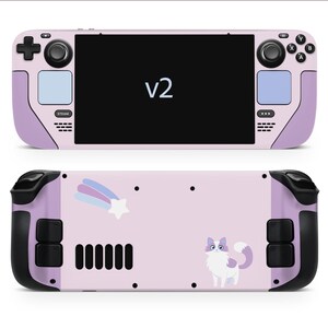 May include: A pink and lavender handheld gaming console with the text "v2" on the screen. The back features a cartoon cat, a shooting star, and a rainbow design. The console has black control buttons and a black screen.