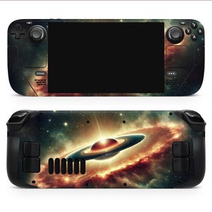 Könnte beinhalten: Ein schwarzes und graues Handheld-Gaming-Gerät mit einem Galaxie-Design. Das Gerät verfügt über einen Bildschirm, Tasten und einen Joystick. Das Galaxie-Design zeigt eine wirbelnde Nebelwolke mit einem hellen Stern in der Mitte.