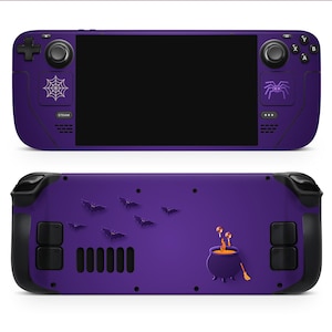 May include: A purple handheld gaming console with black accents. The front features a spiderweb and spider graphic, while the back has bat silhouettes and a cauldron design. The console has a black screen and control buttons.