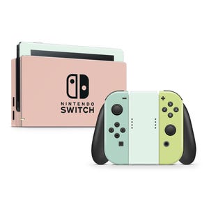 May include: A Nintendo Switch console in a pastel pink color with matching controllers in mint green and lime green. The console has the Nintendo Switch logo in black. The controllers have black joysticks and buttons.