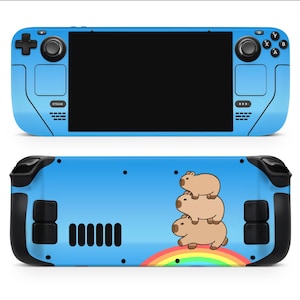 Könnte beinhalten: Eine blaue Handheld-Spielekonsole mit schwarzem Bildschirm und Bedienelementen. Die Rückseite zeigt ein Design von drei gestapelten Capybaras über einem Regenbogen. Die Konsole hat schwarze Akzente und ein Steam-Logo.