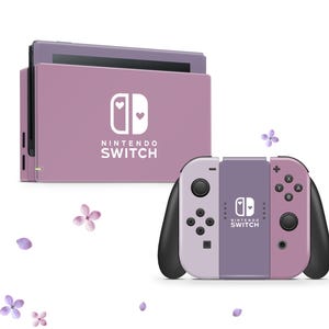 May include: A pink Nintendo Switch console with a white heart design and the text "NINTENDO SWITCH". The console is paired with a matching pink and purple Joy-Con controller.