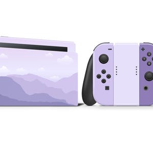 May include: A Nintendo Switch console and controllers with a lavender mountain range design. The console is in a landscape orientation, and the controllers are detached, with black grips and lavender buttons.