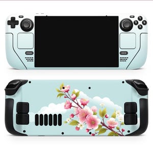 Op de afbeelding: Een lichtblauwe handheld-gameconsole met een bloemenontwerp met roze en witte bloemen. De console heeft zwarte knoppen en een scherm.