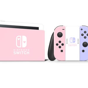 以下が含まれることがあります： ピンク色のNintendo Switch本体とコントローラー。本体はピンク色で、Nintendo Switchのロゴとハートのデザインがあります。コントローラーはピンク、白、ラベンダー色で、黒のアクセントが付いています。「NINTENDO SWITCH」の文字が見えます。