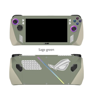 May include: Sage green handheld gaming console with a black screen, buttons, and a logo. The console has a light beige accent color on the sides. The text "ROG" is visible on the screen. The text "Sage green" is below the console.