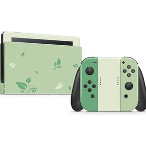 Może przedstawiać: Zielono-biała konsola Nintendo Switch z kwiatowym wzorem. Konsola jest zamknięta, a kontrolery Joy-Con są przymocowane.
