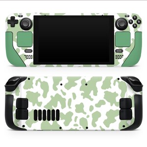 May include: A handheld gaming console with a cow print design. The console has a black screen, green accents, and white spots. The back of the console also has the cow print design. It features buttons, joysticks, and a directional pad.