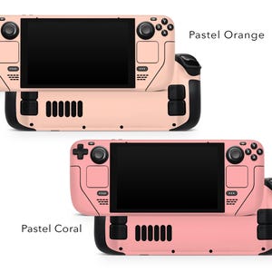 May include: Two handheld gaming consoles in pastel orange and pastel coral colours. Both consoles have black buttons and a black screen.