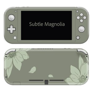 May include: A sage green handheld gaming console with the text "Subtle Magnolia" on the screen. The back of the console features a floral design with large magnolia flowers and leaf accents in a lighter green.