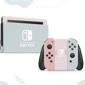 Könnte beinhalten: Eine hellblaue und rosafarbene Nintendo Switch-Konsole mit einem weißen Nintendo Switch-Logo und dem Text "NINTENDO SWITCH". Die Konsole ist in geschlossener Position mit dem Bildschirm nach vorne. Die Konsole steht auf einer weißen Oberfläche. Die Joy-Con-Controller sind an der Konsole befestigt. Die Joy-Con-Controller sind hellblau und rosa. Die Joy-Con-Controller haben ein weißes Nintendo Switch-Logo und den Text "NINTENDO SWITCH".