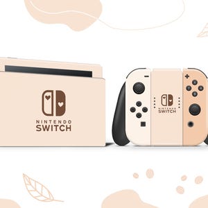 May include: A Nintendo Switch console and controllers in a cream and black color scheme. The console and controllers feature a heart design and the words "Nintendo Switch". The background is white with leaf and abstract shapes.