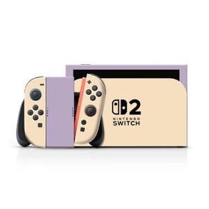 May include: A Nintendo Switch console with a cream-colored body and lavender accents. The Joy-Con controllers are cream and black, with orange and black buttons. The console's screen is lavender, and the dock has the Nintendo Switch logo.