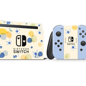 以下が含まれることがあります： レモンとブルーベリーのデザインのカスタムスキンを施したNintendo Switch本体とコントローラー。スキンは薄い黄色で、青と黄色のフルーツのイラストと「Nintendo Switch」の文字が描かれています。