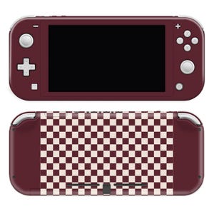 May include: A burgundy handheld gaming console with a black screen and white buttons. The back features a burgundy and cream checkerboard pattern. The console has a sleek, modern design.