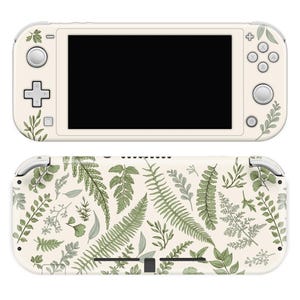 May include: A white Nintendo Switch Lite console with a floral pattern featuring green ferns and leaves on the back. The console has a black screen and white buttons.