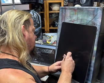Könnte beinhalten: Eine Person mit einem Tattoo, das "Crazy Thing" auf dem Arm steht, arbeitet mit einer Sprühpistole auf einer schwarzen Leinwand. Die Leinwand ist auf einem Holzrahmen montiert. Im Hintergrund befinden sich mehrere andere Leinwände sowie ein Regal mit verschiedenen Gegenständen.