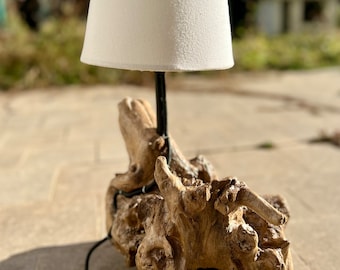 May include: A table lamp with a white fabric shade sits on a natural driftwood base. The lamp has a black cord and plug.