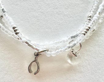 Conjunto de pulsera de cuentas blancas y transparentes con dijes.