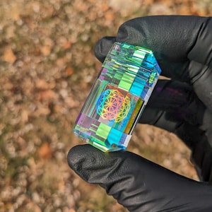 May include: A clear glass prism with a rainbow iridescent finish. The prism has a geometric design inside, with a multi-colored mandala pattern.