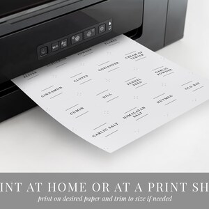 May include: A sheet of printable spice jar labels with a variety of common spices listed, including pepper, cinnamon, cloves, coriander, cream of tartar, cumin, dill, fennel seed, garlic powder, garlic salt, Himalayan salt, nutmeg, and old bay. The labels are printed on a white background with black text. The sheet is being fed into a black printer.