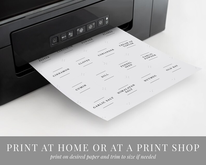 May include: A sheet of printable spice jar labels with a variety of common spices listed, including pepper, cinnamon, cloves, coriander, cream of tartar, cumin, dill, fennel seed, garlic powder, garlic salt, Himalayan salt, nutmeg, and old bay. The labels are printed on a white background with black text. The sheet is being fed into a black printer.