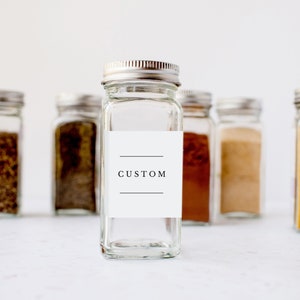 May include: A set of six glass spice jars with silver lids. The centre jar has a white label with the word "CUSTOM" printed on it.