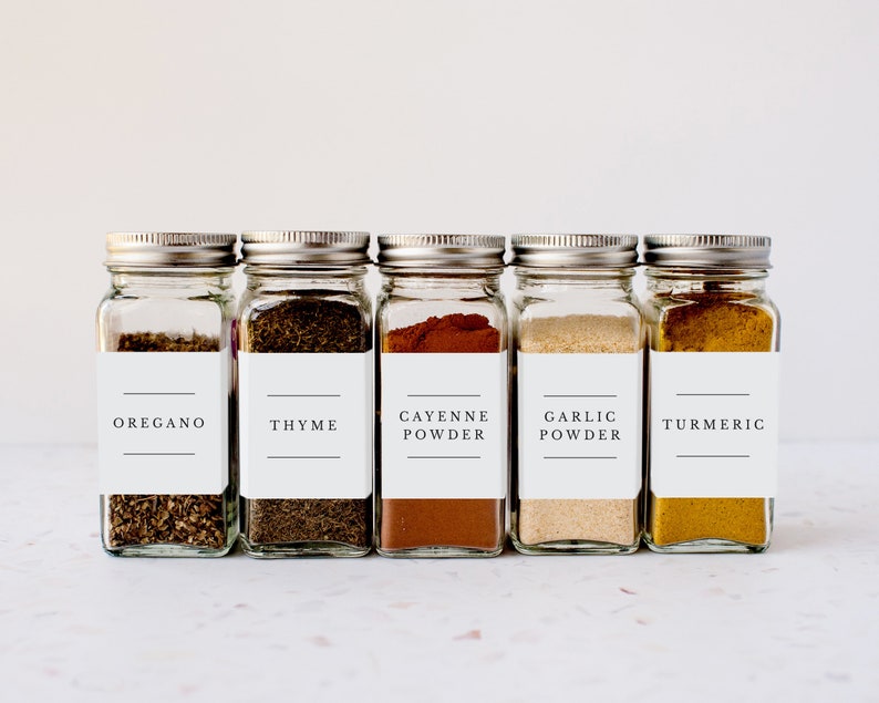 May include: Five glass spice jars with white labels and black text. The labels read "Oregano", "Thyme", "Cayenne Powder", "Garlic Powder", and "Turmeric".
