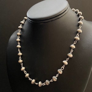 May include: A silver necklace with round beads. The beads are slightly flattened and have a textured surface.