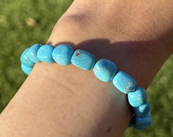May include: A turquoise gemstone bracelet with smooth, rounded beads. The bracelet is worn on a person's wrist.