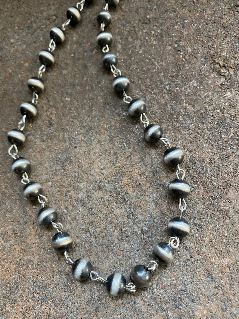May include: A black and white beaded necklace with silver chain links. The beads are round and have a striped pattern.