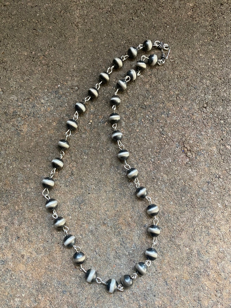 May include: A black and white beaded necklace with a silver clasp. The beads are round and have a striped pattern.