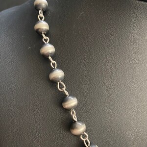 May include: A silver necklace with round, dark grey beads and silver chain links.