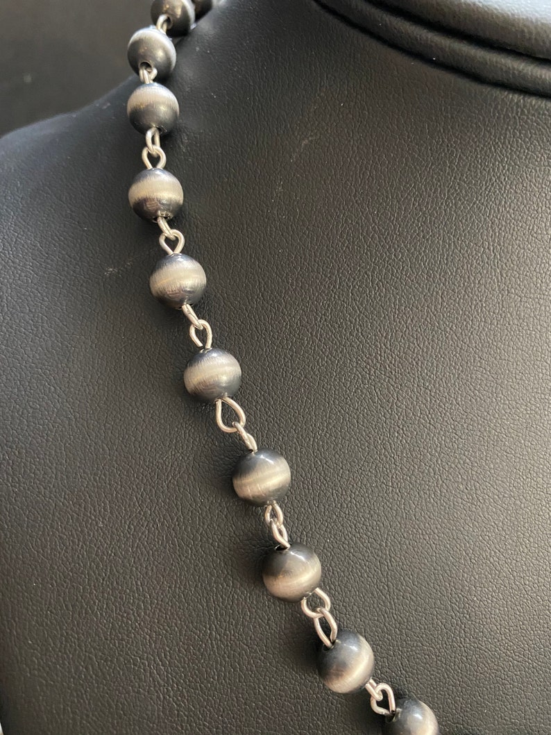 May include: A silver necklace with round, dark grey beads and silver chain links.