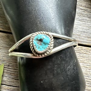 Puede incluir: Una pulsera de plata con una piedra turquesa. La piedra turquesa ovalada está engastada en un bisel decorativo. La pulsera tiene un diseño sencillo y elegante, ideal para el uso diario.