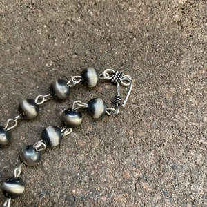 May include: A silver necklace with round beads and a silver clasp. The beads are a dark grey colour with a silver sheen.