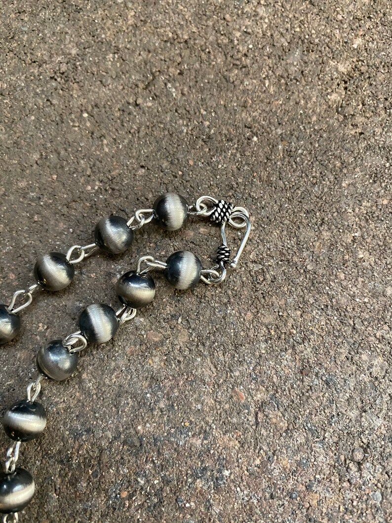 May include: A silver necklace with round beads and a silver clasp. The beads are a dark grey colour with a silver sheen.