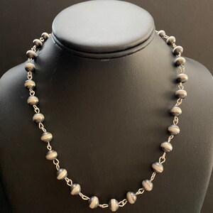 May include: A silver necklace with round beads. The beads are dark grey with a silver stripe around the middle.