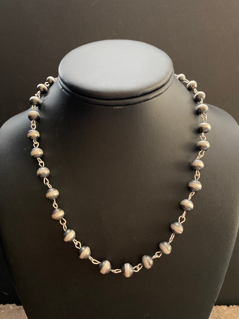 May include: A silver necklace with round beads. The beads are dark grey with a silver stripe around the middle.