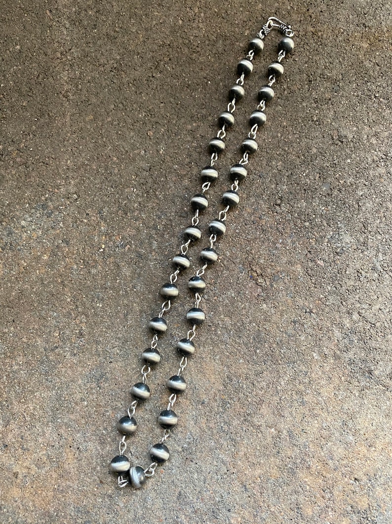 May include: A silver chain necklace with black and white beads. The beads are round and have a smooth, polished finish.