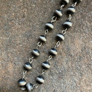 May include: A silver chain necklace with black and silver beads. The beads have a striped pattern.