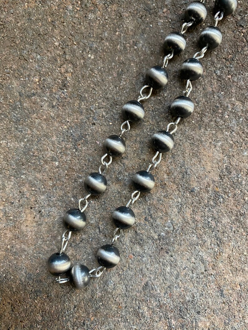 May include: A silver chain necklace with black and silver beads. The beads have a striped pattern.
